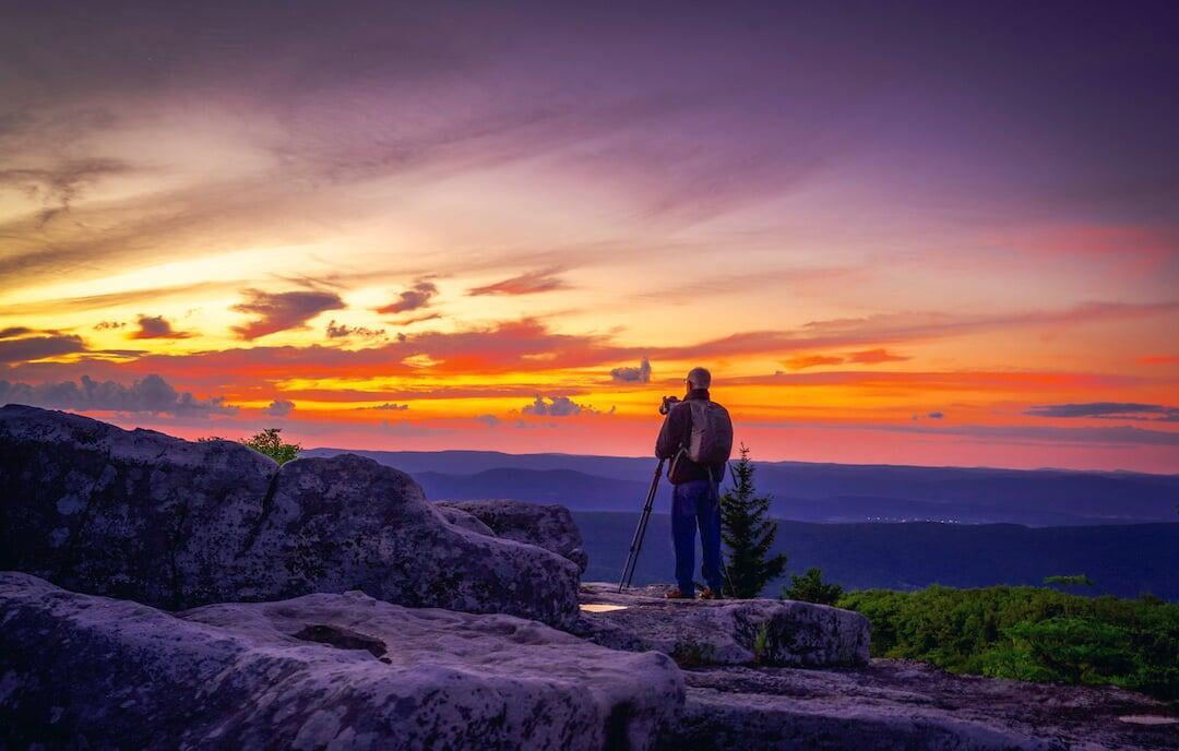 Photograph of a photographer making a photograph of a sunrise from a rock outcropping
